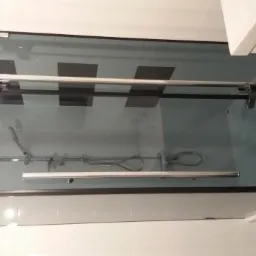 Szklana kabina prysznicowa z czarnymi detalami i chromowanymi uchwytami, widoczna armatura wewnątrz, białe płytki na ścianach i ciemna podłoga.