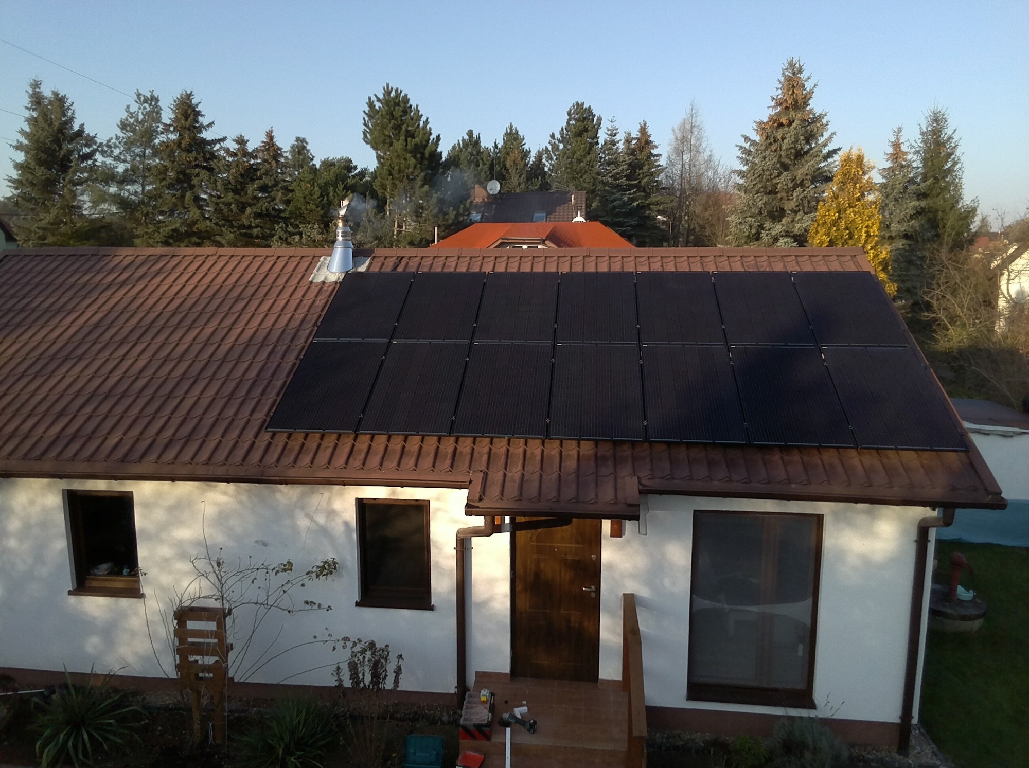 Dom jednorodzinny z brązowym dachem, na którym zamontowane są panele fotowoltaiczne, widok z góry, na pierwszym planie narzędzia instalacyjne