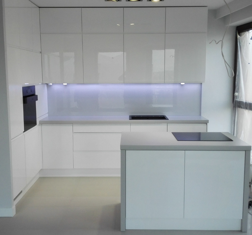 Nowoczesna, biała kuchnia z wyspą w Lublinie, oświetlenie LED podszafkowe, minimalistyczny design, okno częściowo zasłonięte folią ochronną.