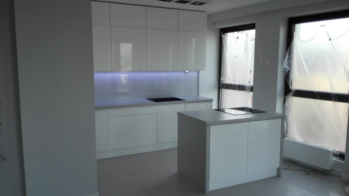 Nowoczesna, biała kuchnia z wyspą, minimalistyczny design, podświetlenie LED nad blatem, okna zabezpieczone folią ochronną podczas remontu.
