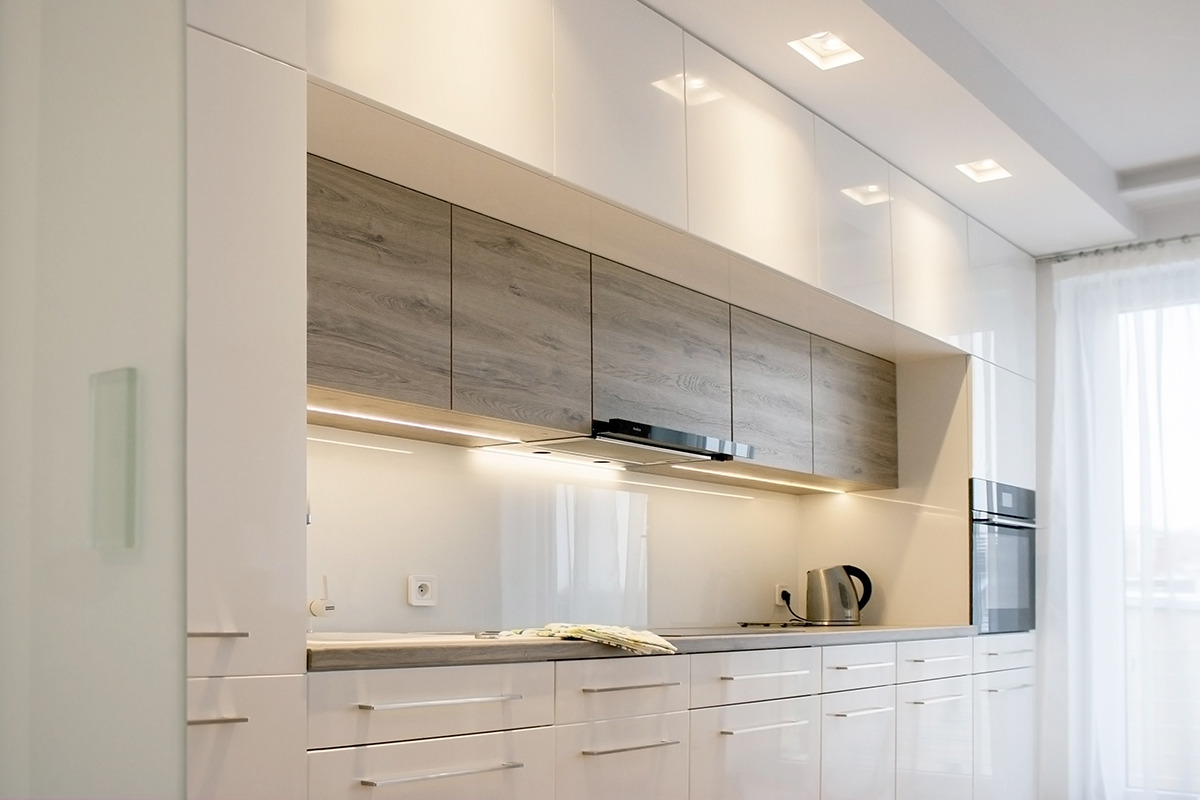 Biała kuchnia z górnymi szafkami w odcieniach szarości imitujących drewno, podświetleniem LED podszafkowym i minimalistycznymi uchwytami.