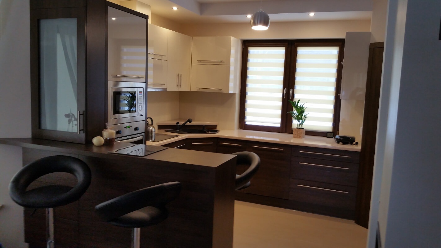 Nowoczesna kuchnia z barkiem, fronty szafek w kolorze ecru i ciemnego brązu, okno z żaluzjami poziomymi, oświetlenie punktowe i wisząca lampa.