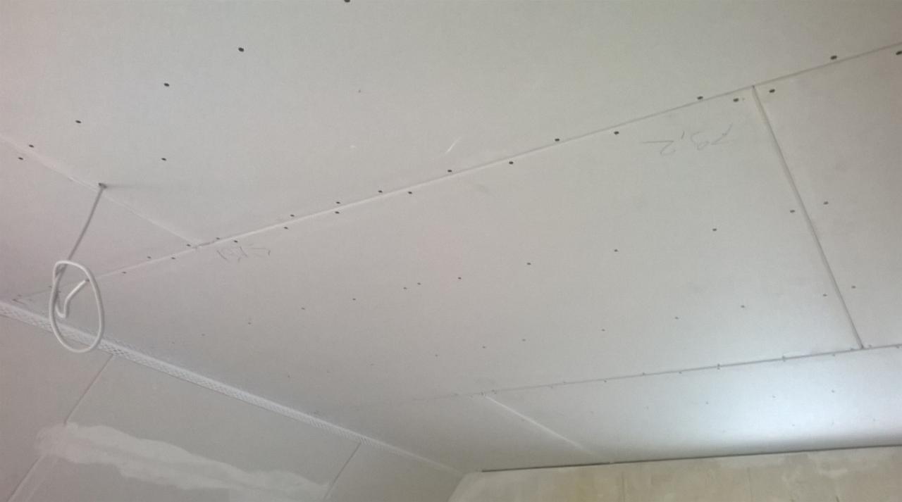 Sufit z płyt kartonowo-gipsowych, widoczne ślady po wkrętach, z zaznaczonymi wymiarami i wystającym przewodem elektrycznym.