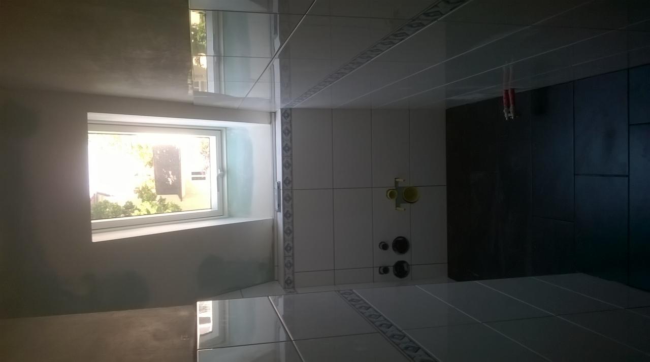 Łazienka w trakcie remontu: białe i ciemne płytki, okno z widokiem na zieleń, przygotowane punkty instalacyjne na ścianie.