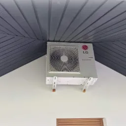 Zamontowana klimatyzacja LG Smart Inverter na białej ścianie pod szarym, skośnym sufitem z desek.