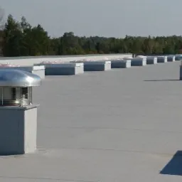 Widok z góry na płaski dach budynku komercyjnego w Bydgoszczy z zamontowanymi kominami wentylacyjnymi z metalowymi daszkami i kratkami ochronnymi.