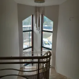 Klatka schodowa z marmurowymi schodami, metalową balustradą i nowoczesną lampą wiszącą, widok przez okno na zewnątrz.