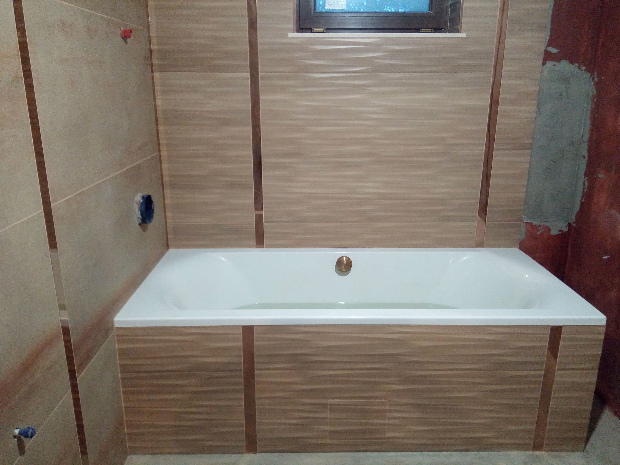 Wanna obudowana płytkami imitującymi drewno, zamontowana w łazience z częściowo wykończonymi ścianami i oknem.