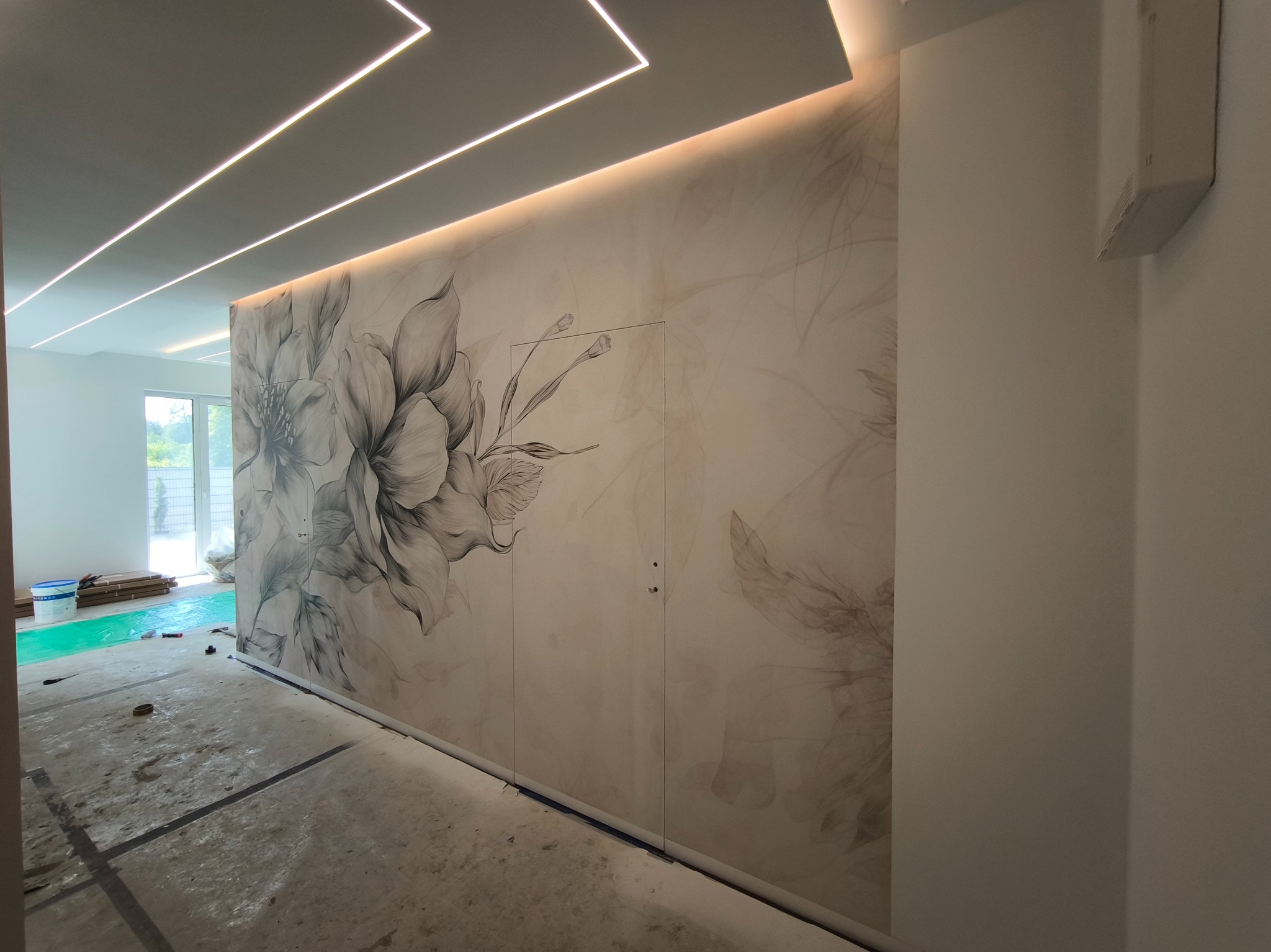 Wnętrze w trakcie wykończenia z ozdobną ścianą z motywem kwiatowym i nowoczesnym oświetleniem LED na suficie.