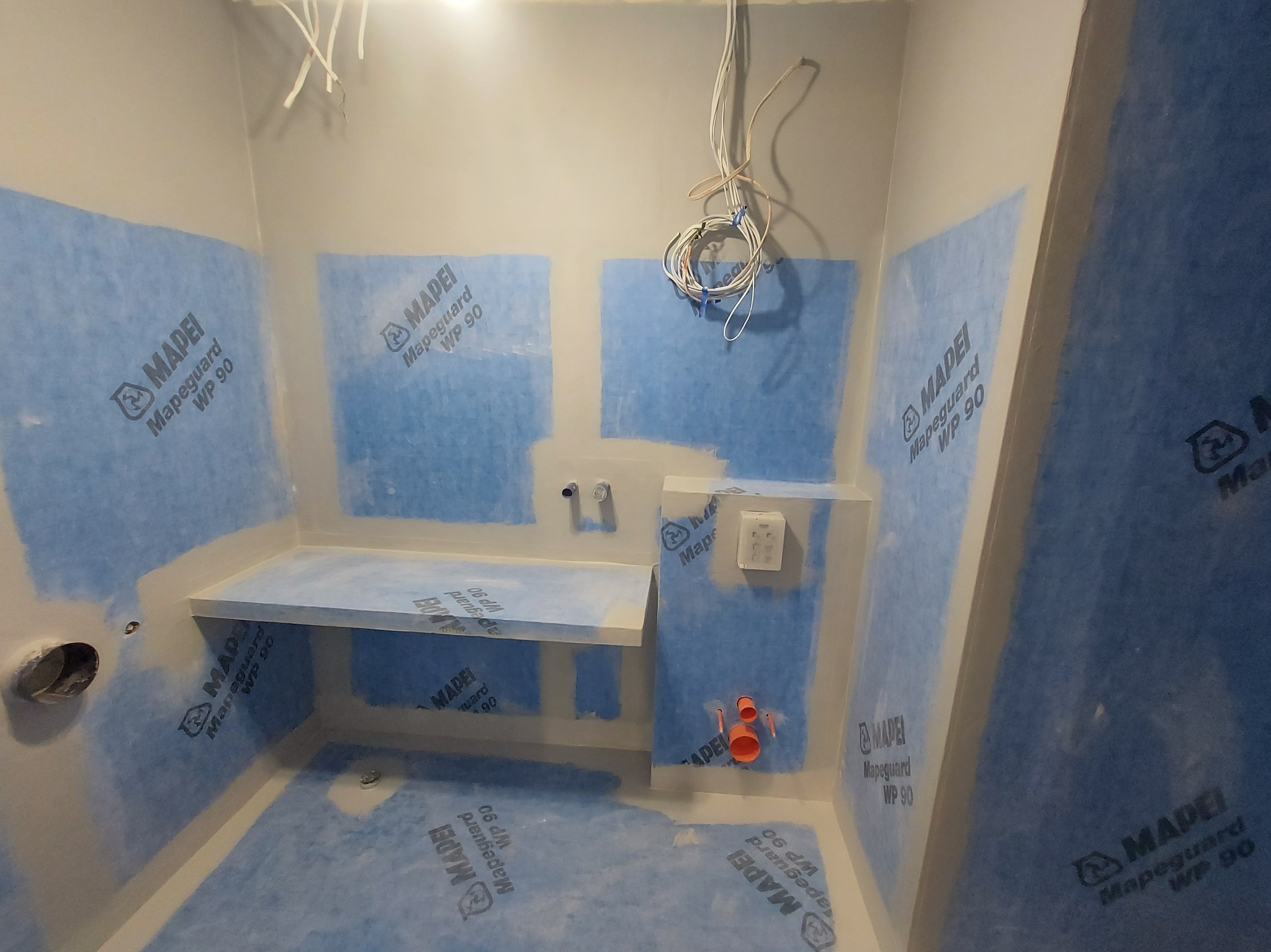 Przygotowanie do hydroizolacji ścian i podłogi w łazience, widoczne materiały Mapei Mapeguard WP 90, instalacja elektryczna i hydrauliczna w trakcie montażu.