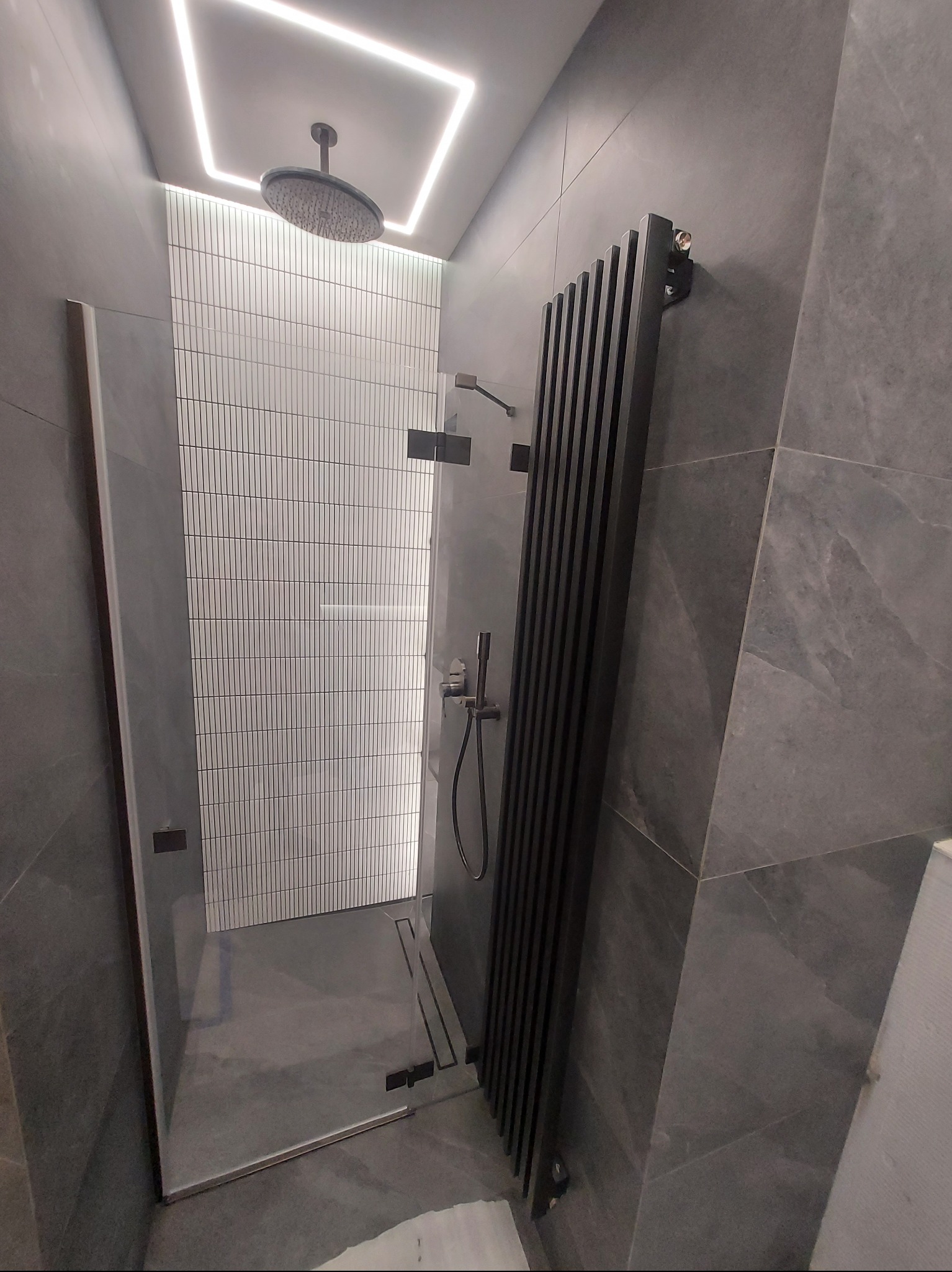Nowoczesna kabina prysznicowa z deszczownicą, wykończona szarymi płytkami i ozdobnym grzejnikiem drabinkowym.