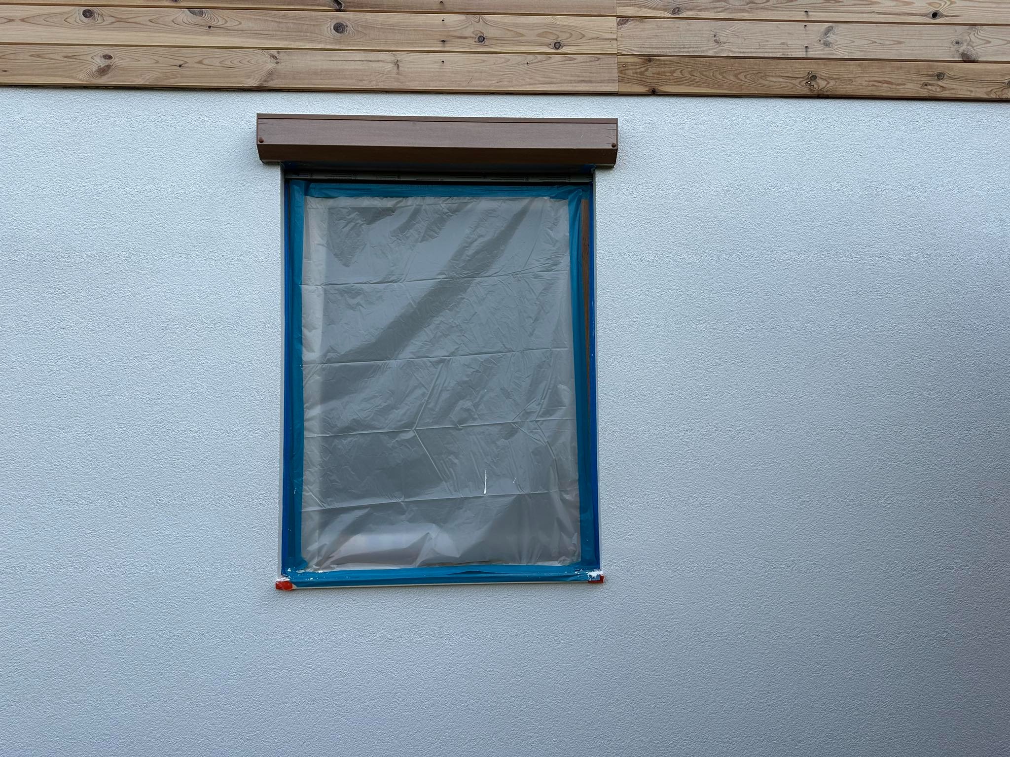 Okno zabezpieczone folią i taśmą malarską na elewacji budynku przed pracami wykończeniowymi.