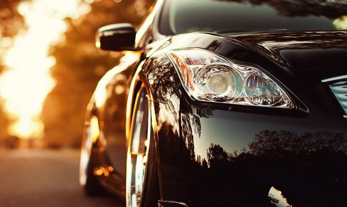 Błyszczący czarny samochód z chromowanymi felgami, uchwycony w ciepłym, zachodzącym słońcu, odbijającym się w lakierze i reflektorach.