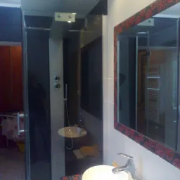 Nowoczesna łazienka z kabiną prysznicową typu walk-in, umywalką na blacie z mozaiką i lustrem w ozdobnej ramie z czerwonym wzorem.