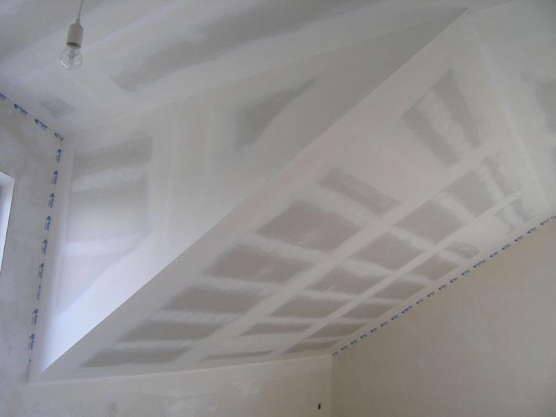 Sufit poddasza z zamontowaną płytą kartonowo-gipsową, z widoczną konstrukcją nośną i szpachlowaniem łączeń, zabezpieczony taśmą malarską przy ścianach.