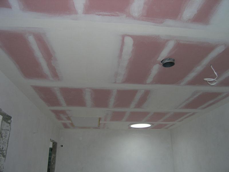 Sufit z widoczną konstrukcją z profili i częściowo przykrytą różową płytą, przygotowany do szpachlowania łączeń, z widocznym otworem na oświetlenie i otworem rewizyjnym.