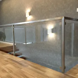 Nowoczesne wnętrze z szklaną balustradą i metalową ramą, oświetlone kinkietami na szarej ścianie, widok na drewniane schody i podłogę z paneli imitujących drewno.