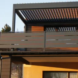 Nowoczesny balkon z szarą, poziomą balustradą i pergolą z regulowanymi lamelami, widok z dołu na tle drzew