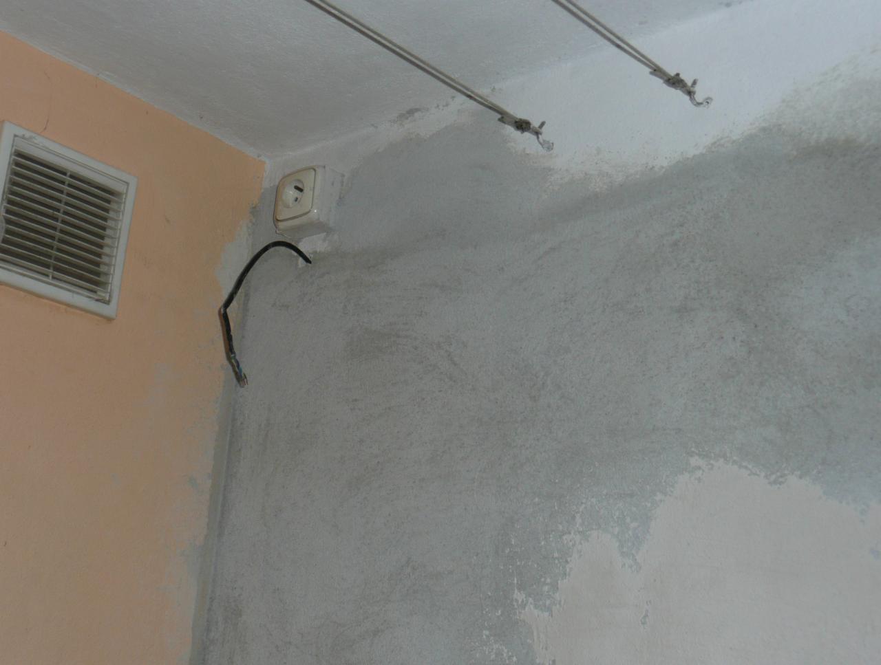 Fragment ściany w trakcie prac wykończeniowych: szpachlowana powierzchnia, wystający kabel elektryczny obok gniazdka, kratka wentylacyjna na sąsiedniej ścianie.
