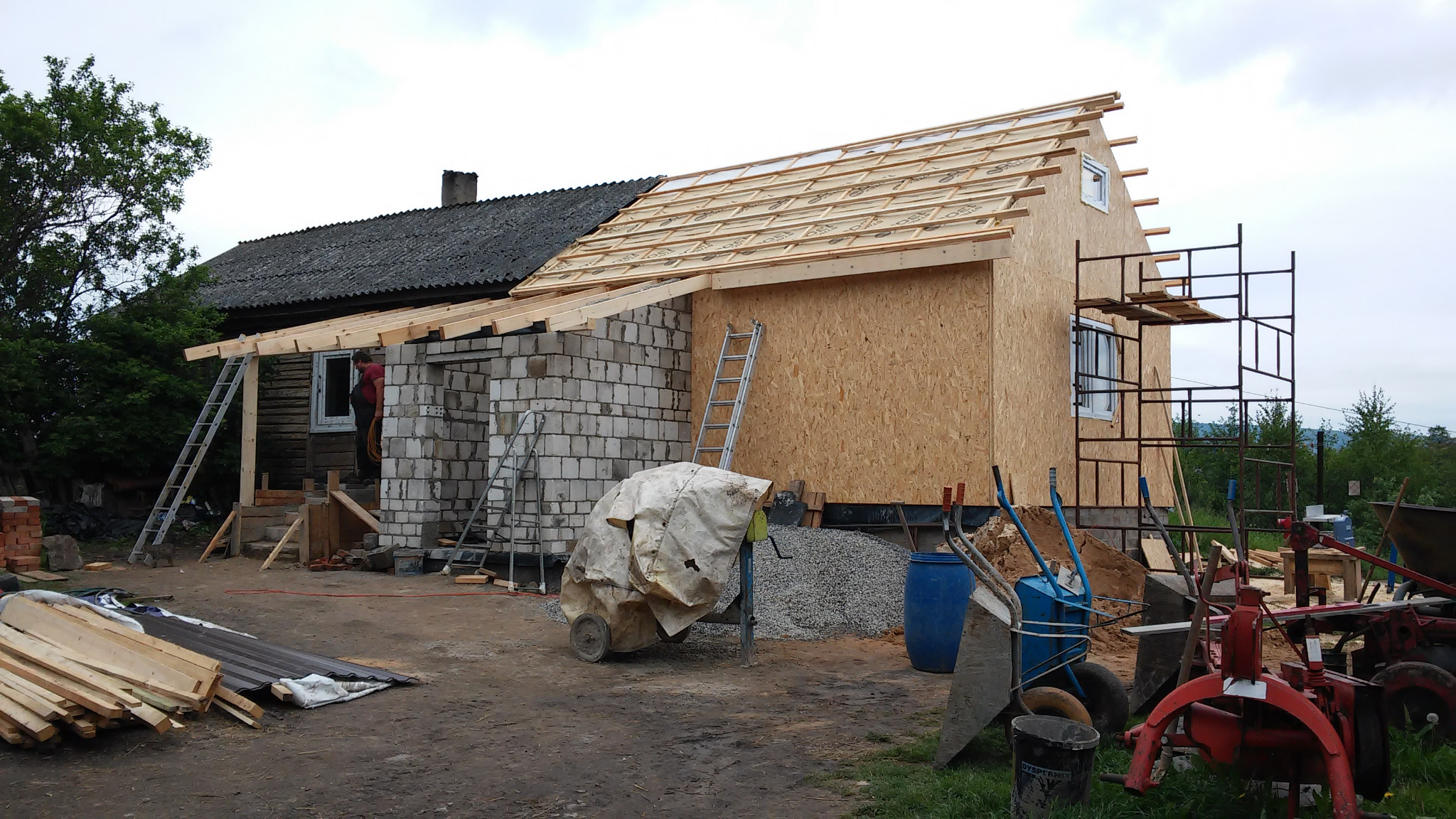 Budowa domu: widok na konstrukcję z drewna i bloczków, częściowo zadaszoną, z widocznymi narzędziami i materiałami budowlanymi.