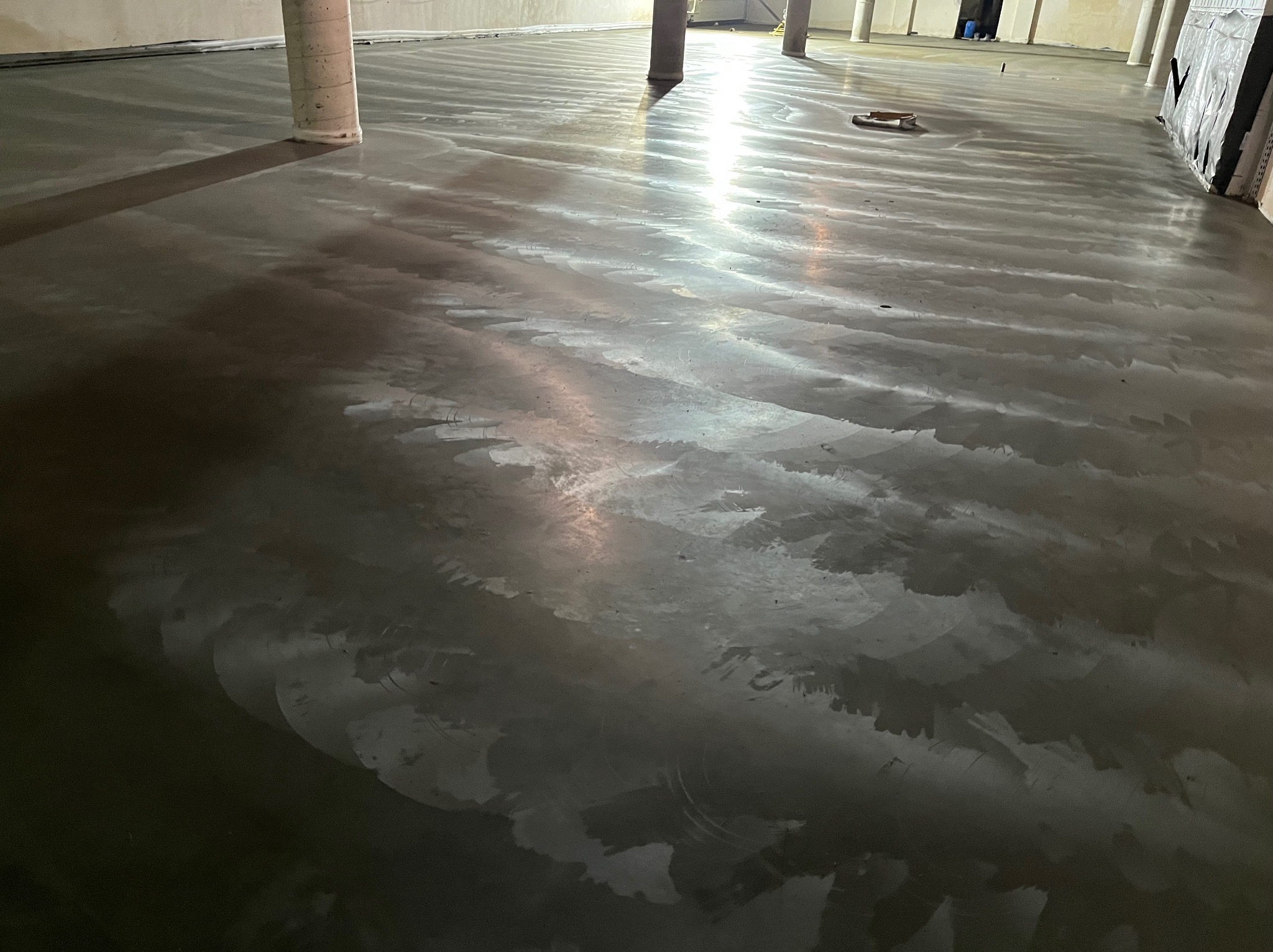 Świeżo wylana, błyszcząca posadzka w dużym pomieszczeniu z kolumnami, widoczne ślady po narzędziach wygładzających.