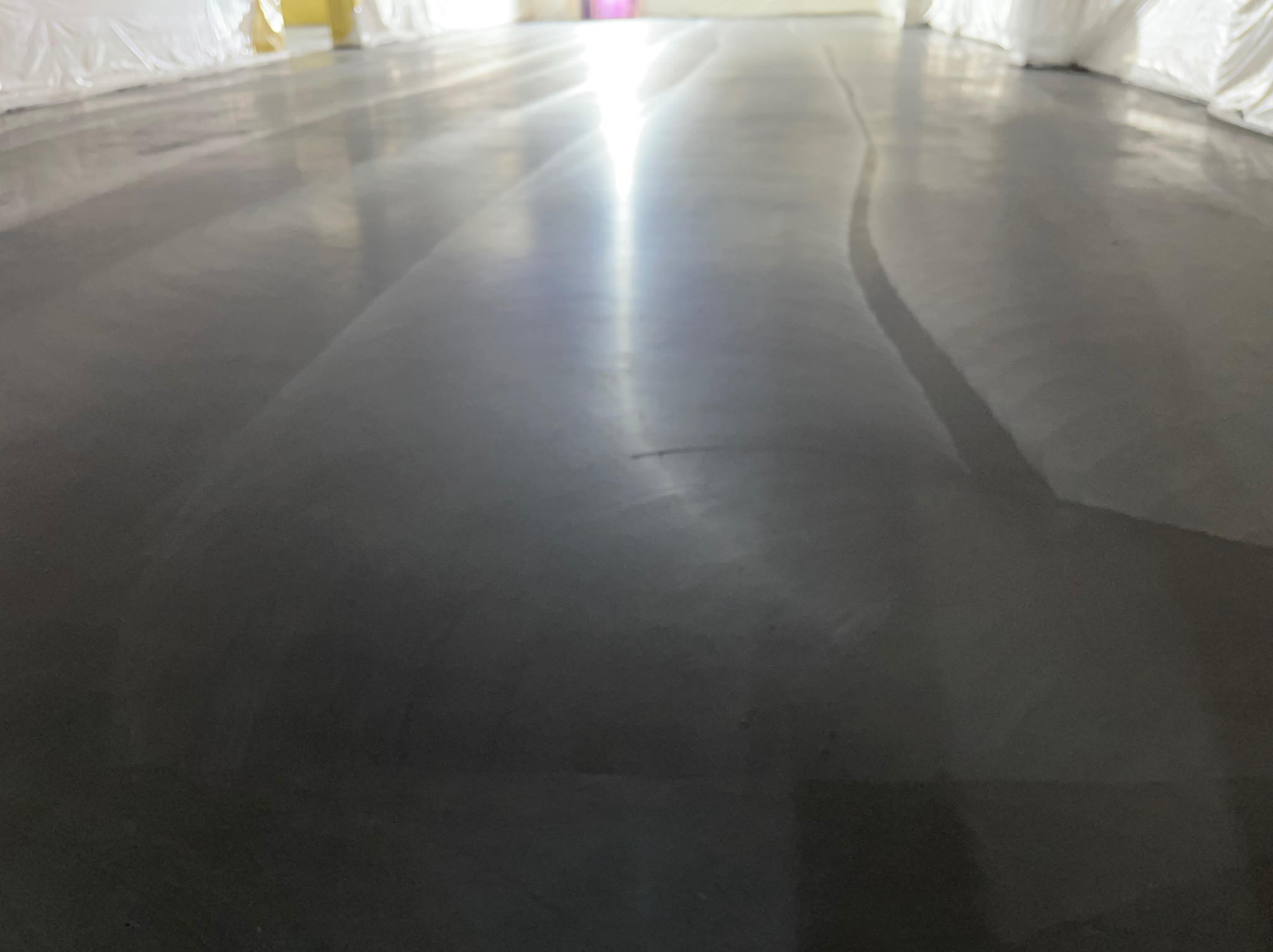 Świeżo wylana, szara, błyszcząca posadzka w hali przemysłowej z widocznymi śladami po rozprowadzaniu masy.