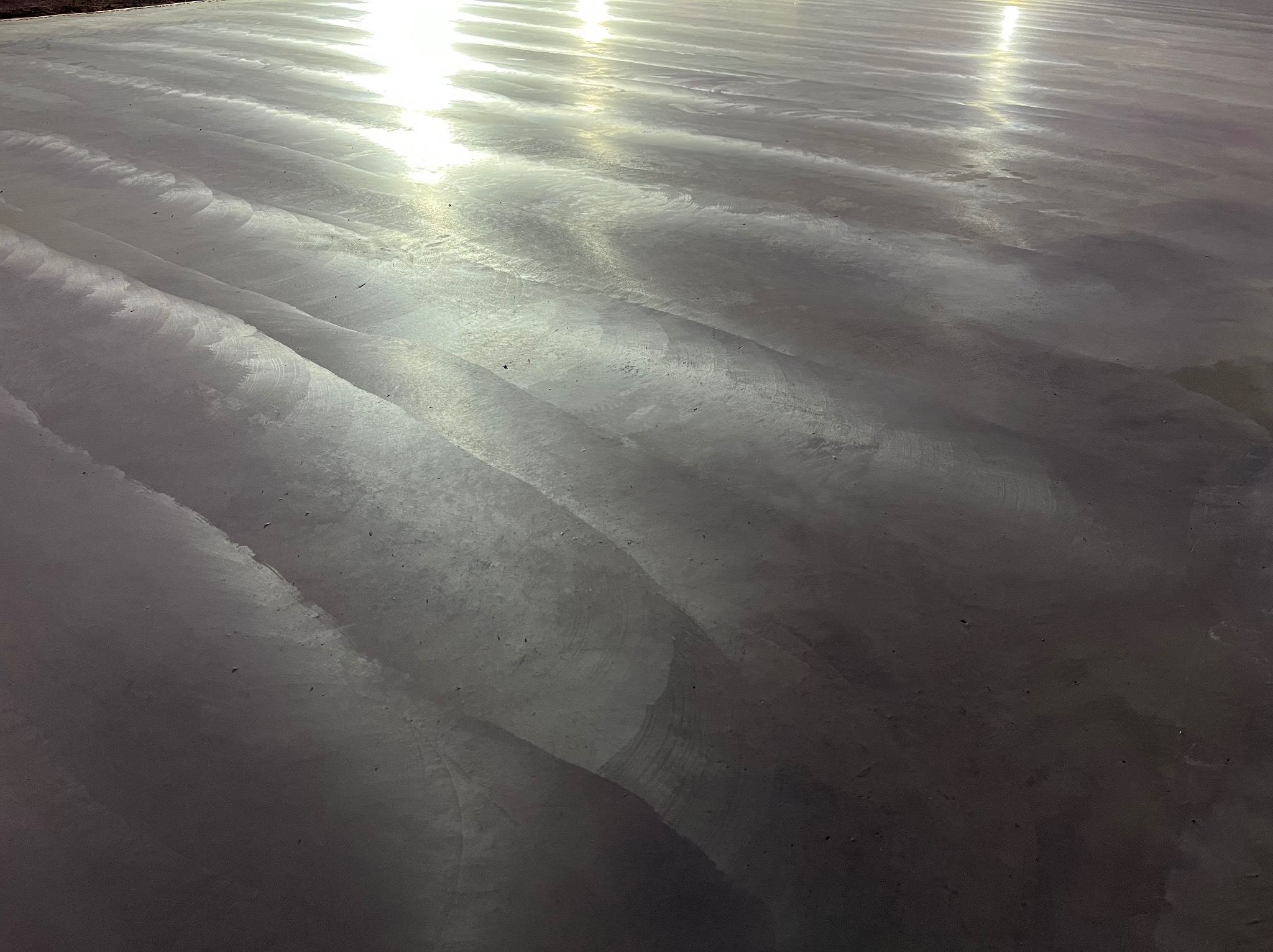 Świeżo wylana, błyszcząca, szara posadzka z widocznymi śladami po narzędziach i odbiciami światła.