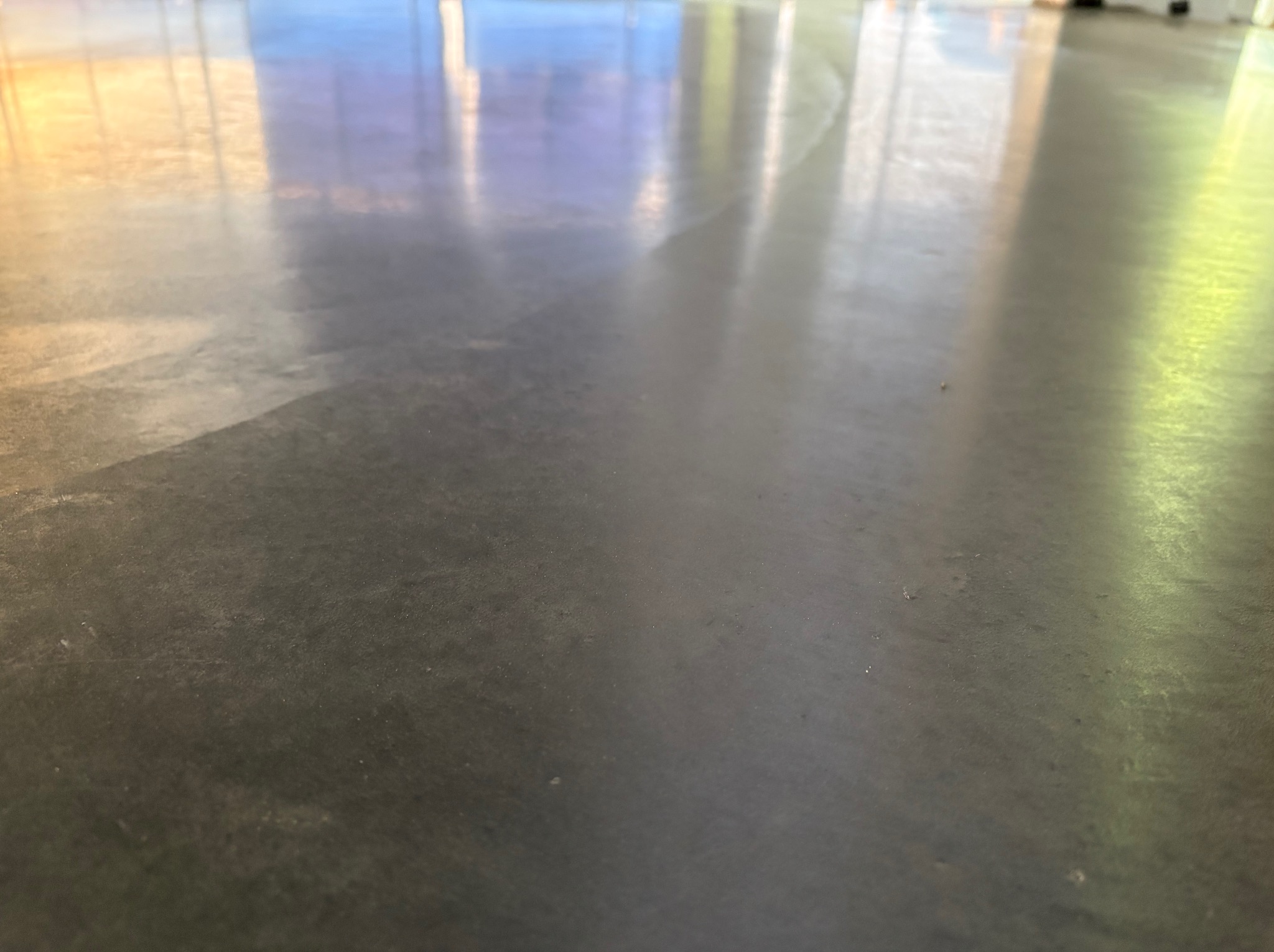Szara, wypolerowana powierzchnia betonowa z refleksami światła słonecznego wpadającego przez okno.