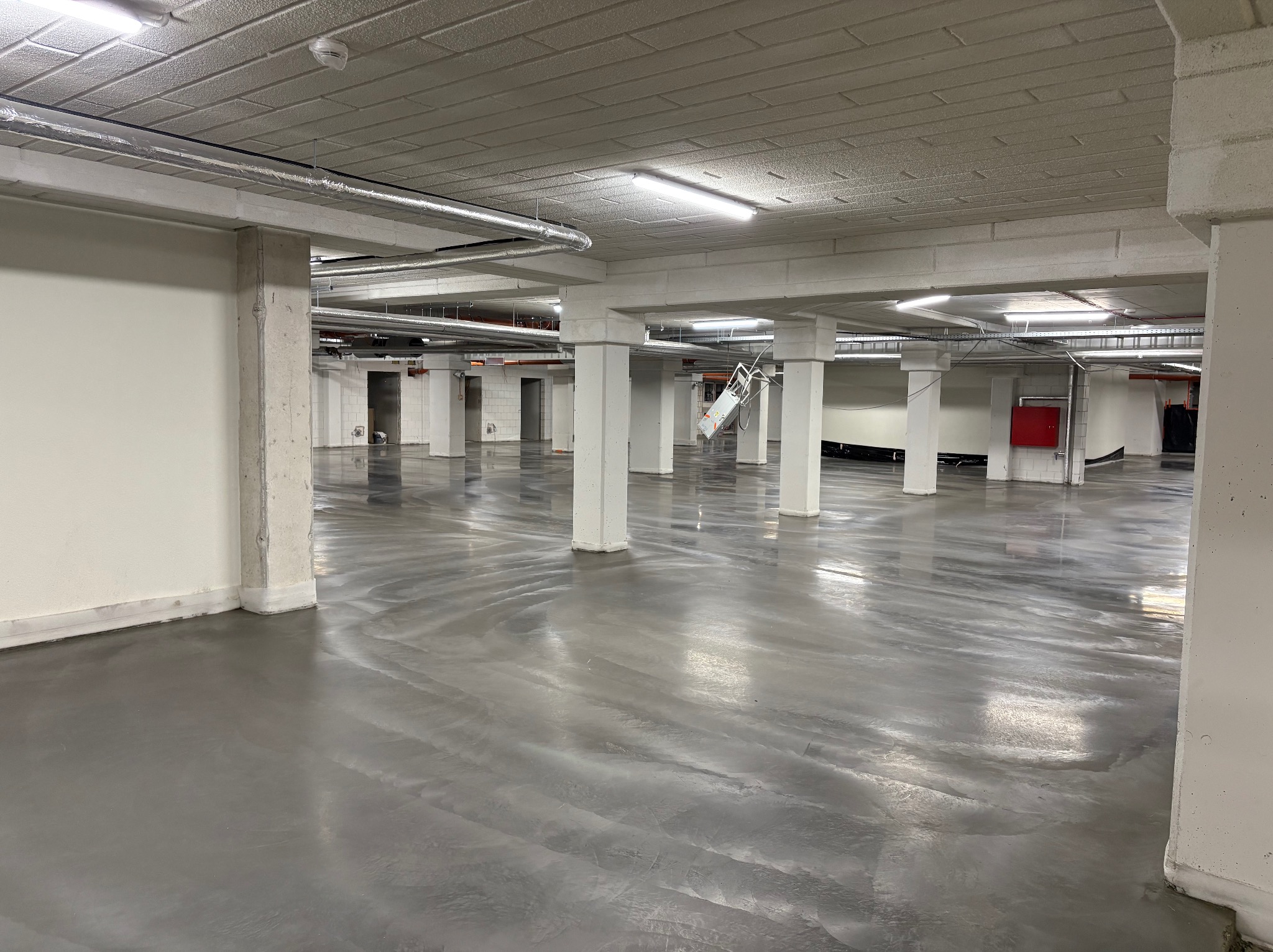 Gładka, szara posadzka przemysłowa w hali magazynowej ze słupami w Szczutowie. Widoczne instalacje pod sufitem i oświetlenie. Nowoczesne wykończenie podłogi.