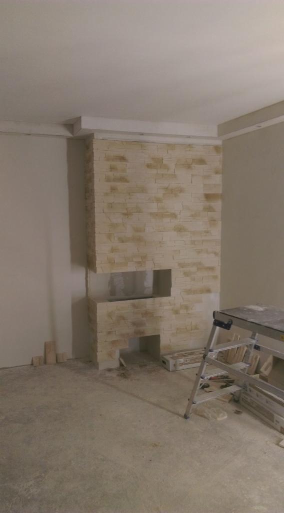 Wnętrze w Ustce z fragmentem ściany wykończonym płytkami imitującymi kamień, z widocznymi otworami i drabinką malarską w tle, sugerujące prace wykończeniowe.