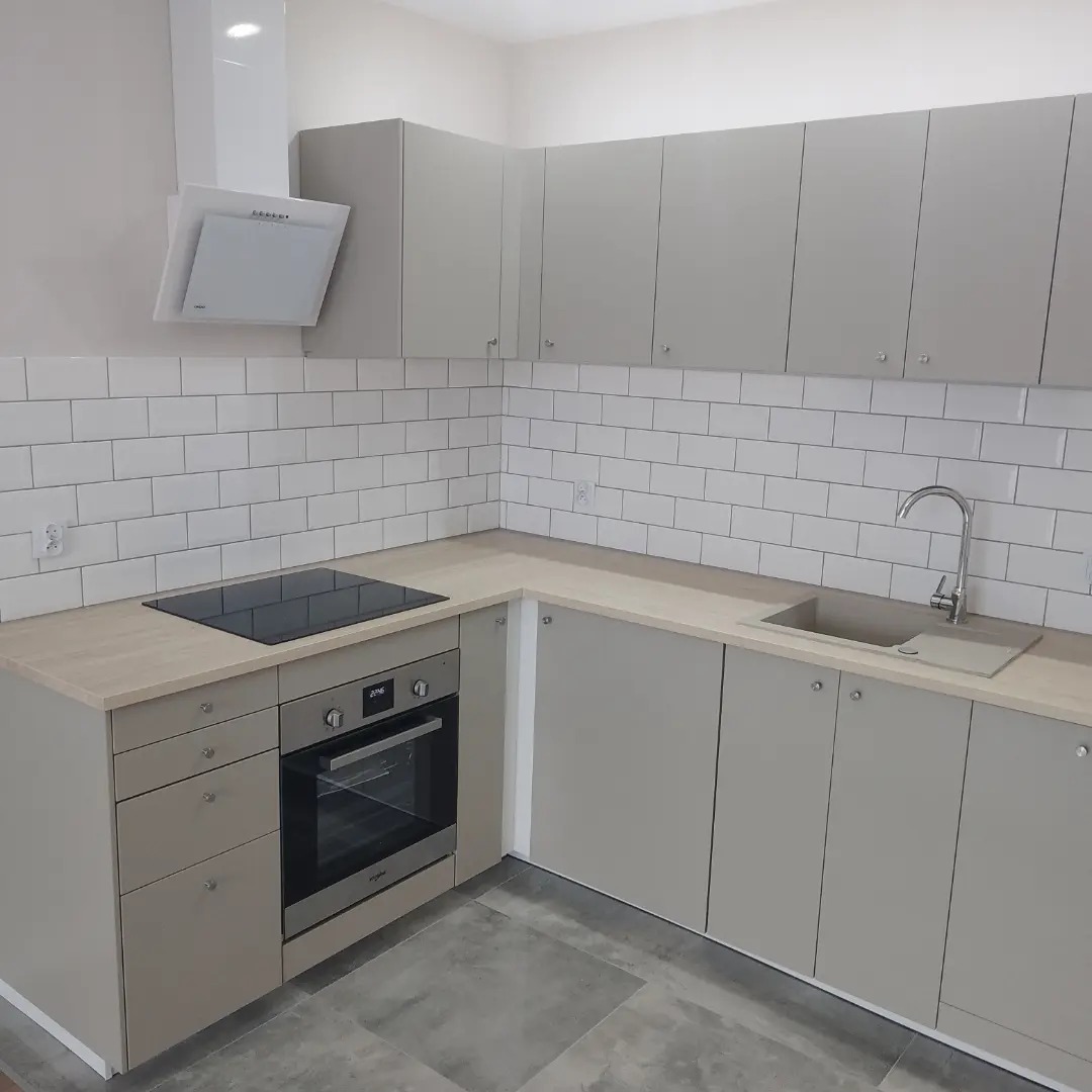 Jasnoszara kuchnia z białymi kaflami na ścianie, widoczna płyta indukcyjna, piekarnik, zlew i okap, minimalistyczny design.