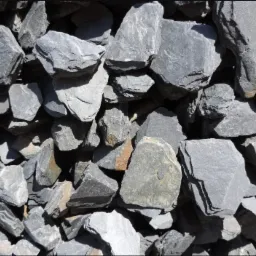 Stos szarego, łupanego żwiru o nieregularnych kształtach, oświetlonego z góry, z widocznymi krawędziami i teksturą kamienia.