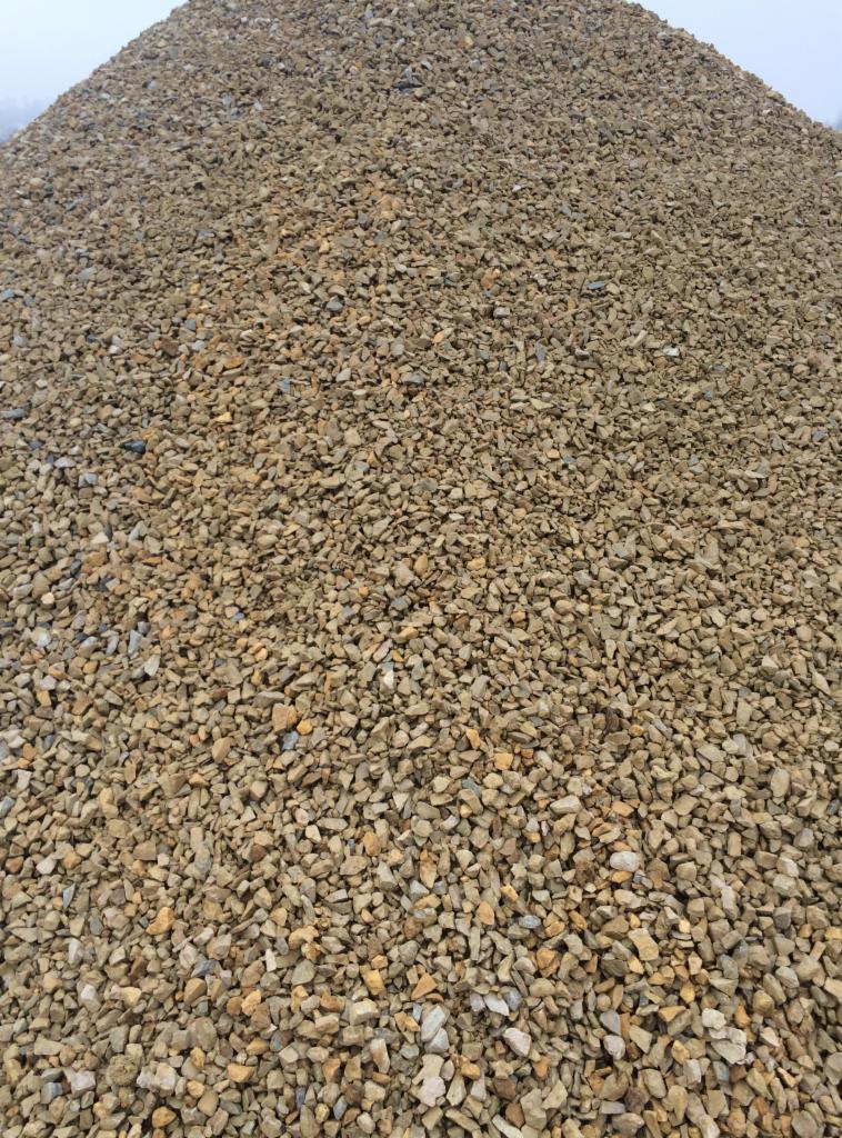 Duża pryzma drobnych, brązowo-szarych kamieni o nieregularnych kształtach, widoczna z bliska, z rozmytym tłem nieba.