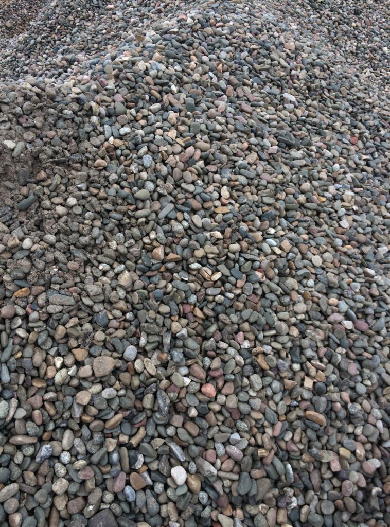 Kupa drobnych, okrągłych kamieni w odcieniach szarości, brązu i różu, z widocznym fragmentem ziemi po lewej stronie.