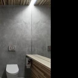 Decco - Minimalistyczna łazienka z betonową ścianą, drewnianym sufitem i blatem umywalkowym z listewek; wisząca toaleta i ukryta spłuczka.