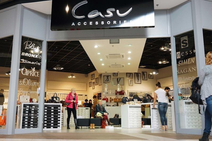 Widok na wnętrze sklepu z akcesoriami odzieżowymi Casu Accessories z klientami w środku, widoczne półki z torebkami i butami oraz napisy marek na witrynach.