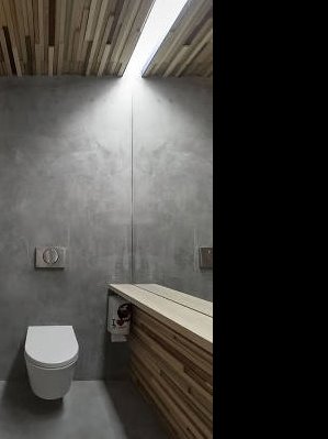 Minimalistyczna łazienka z betonową ścianą, drewnianym sufitem i blatem umywalkowym z listewek; wisząca toaleta i ukryta spłuczka.