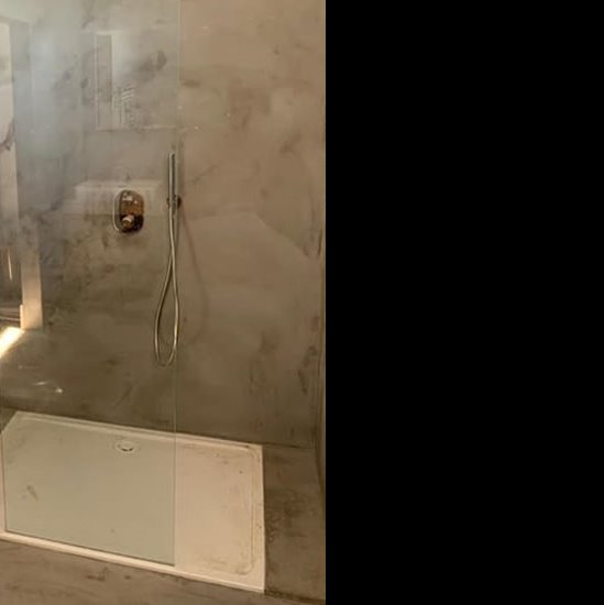 Kabina prysznicowa z szarą, imitującą beton ścianą i białą brodzikiem, widoczne ślady użytkowania.