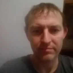 Portret mężczyzny w szarej koszulce na tle jasnej ściany.