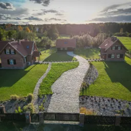 Widok z lotu ptaka na posesję z trzema domami, brukowaną ścieżką z kostki granitowej, zadbanym trawnikiem i ozdobnymi rabatami.