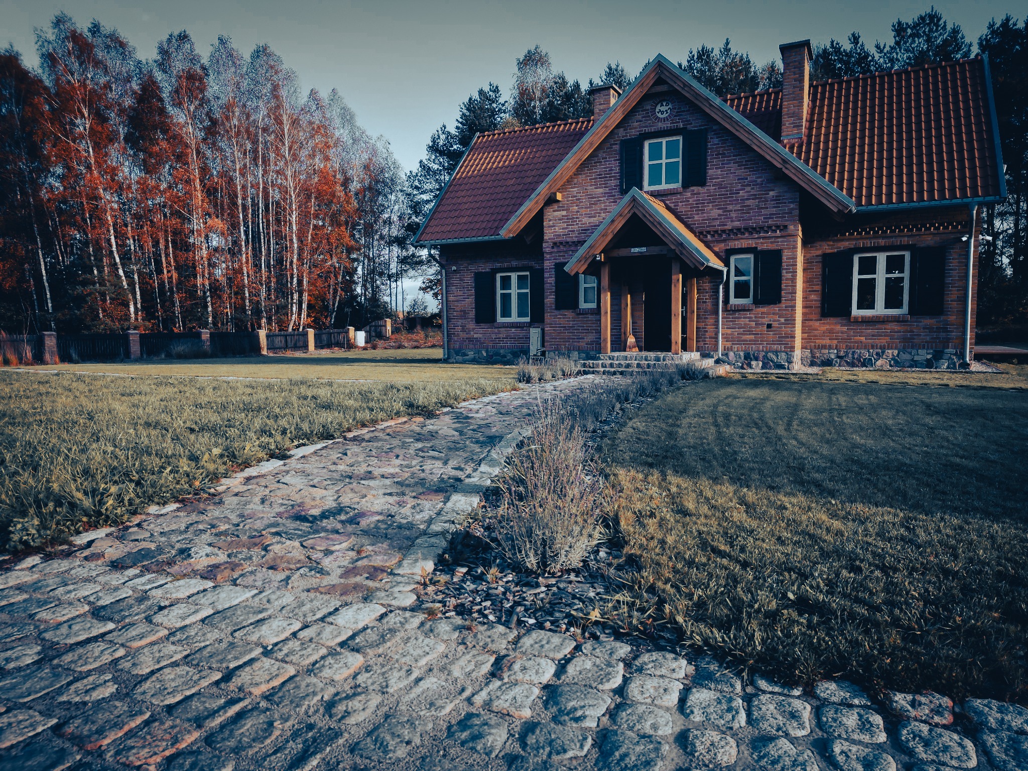 Dom z czerwonej cegły z brukowaną ścieżką i jesiennymi drzewami w tle.