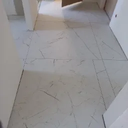 Ułożona podłoga z płytek imitujących marmur w korytarzu, widoczne niedokończone prace wykończeniowe przy listwach przypodłogowych.
