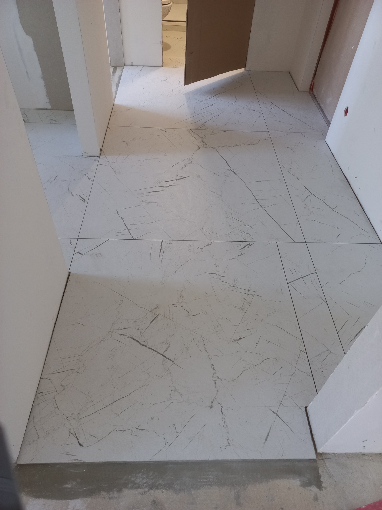 Ułożona podłoga z płytek imitujących marmur w korytarzu, widoczne niedokończone prace wykończeniowe przy listwach przypodłogowych.