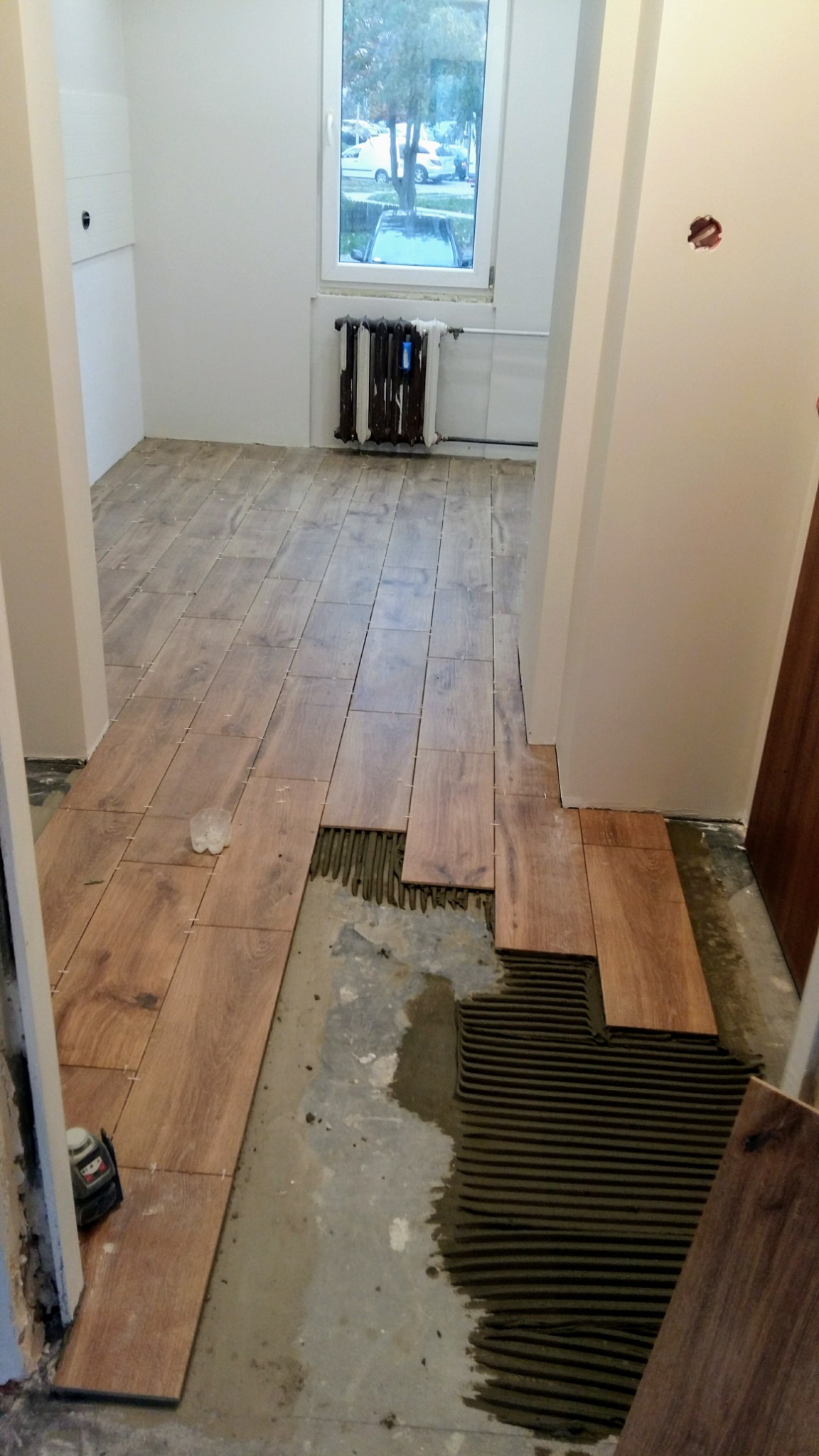 Układanie drewnopodobnych płytek podłogowych w korytarzu, widoczny laser krzyżowy do poziomowania i resztki kleju na podłodze.