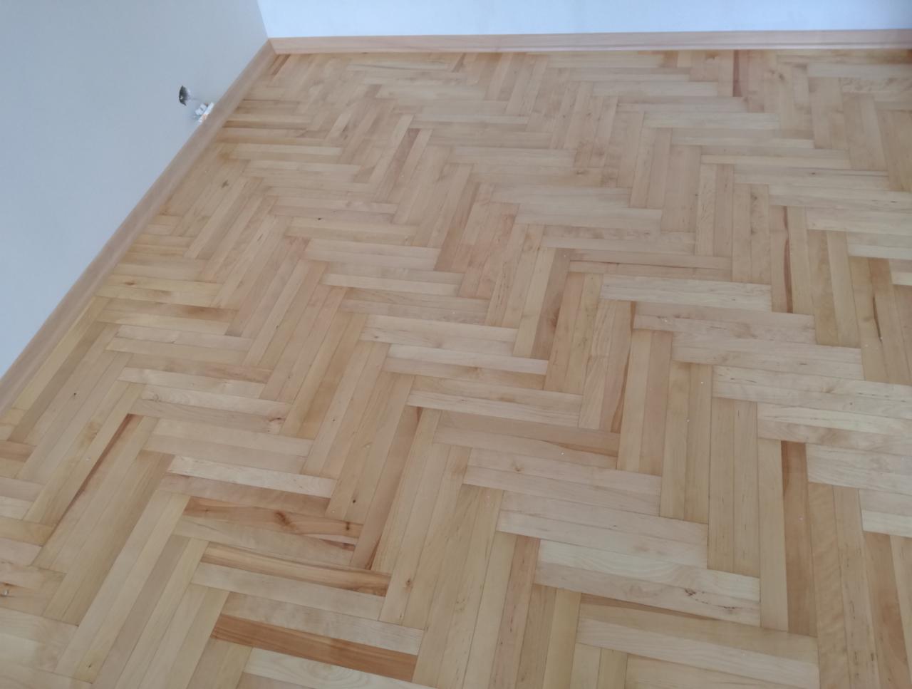 Jasny, drewniany parkiet ułożony w jodełkę, widok z góry, świeżo po lakierowaniu z widocznymi refleksami światła.