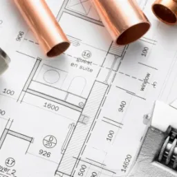 Miedziane rury, wężyki w oplocie stalowym i klucz nastawny leżące na planie instalacji wodno-kanalizacyjnej.