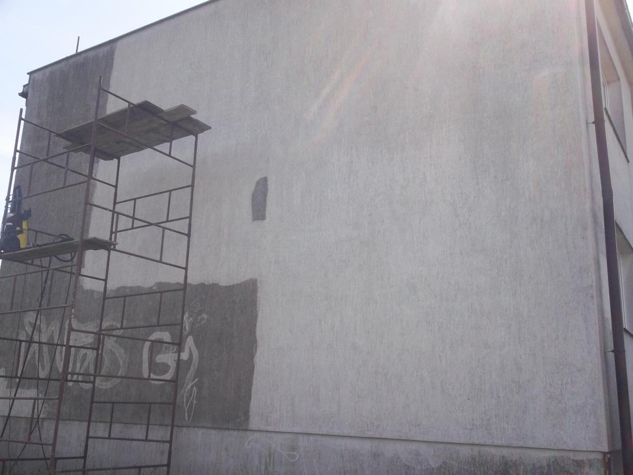 Fragment budynku z widocznymi śladami po usunięciu graffiti i częściowo odnowioną elewacją, rusztowanie z myjką ciśnieniową w lewym dolnym rogu.