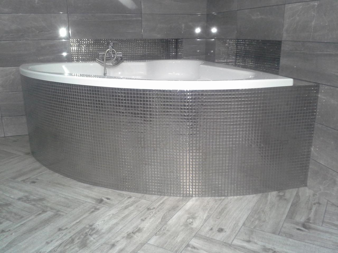 Nowoczesna, narożna wanna obudowana mozaiką w odcieniach szarości, dopasowana kolorystycznie do płytek ściennych i podłogowych imitujących drewno.