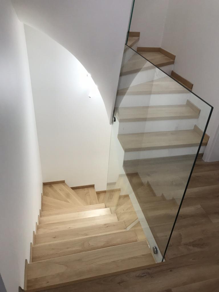 Jasne drewniane schody z przezroczystą szklaną balustradą, widok z góry, minimalistyczny design.