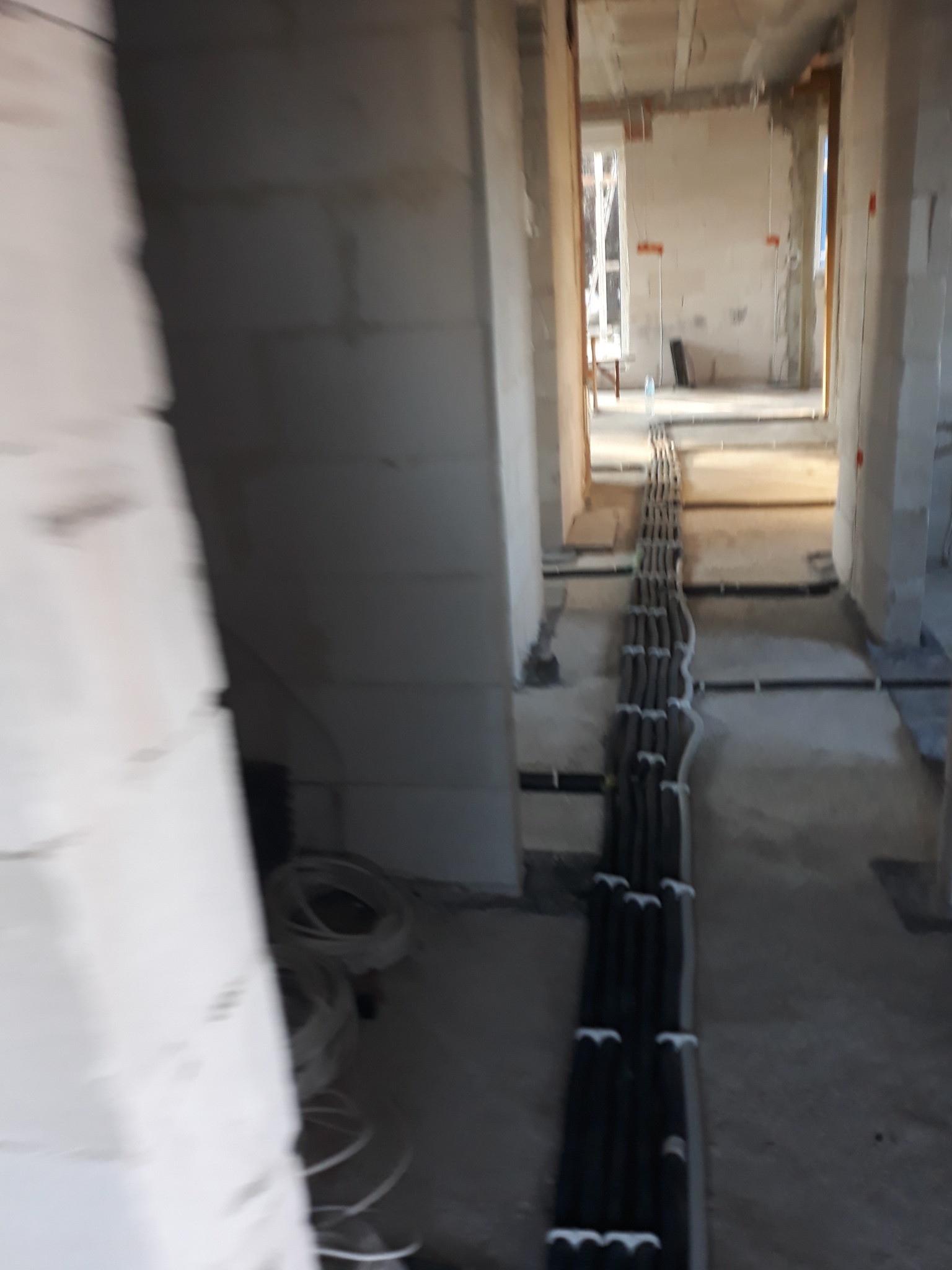 Wnętrze w stanie surowym z widocznymi przewodami elektrycznymi ułożonymi w korytku na podłodze, prowadzącymi przez kilka pomieszczeń.